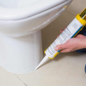 Caulking around a toilet after installation in Troy, Michigan